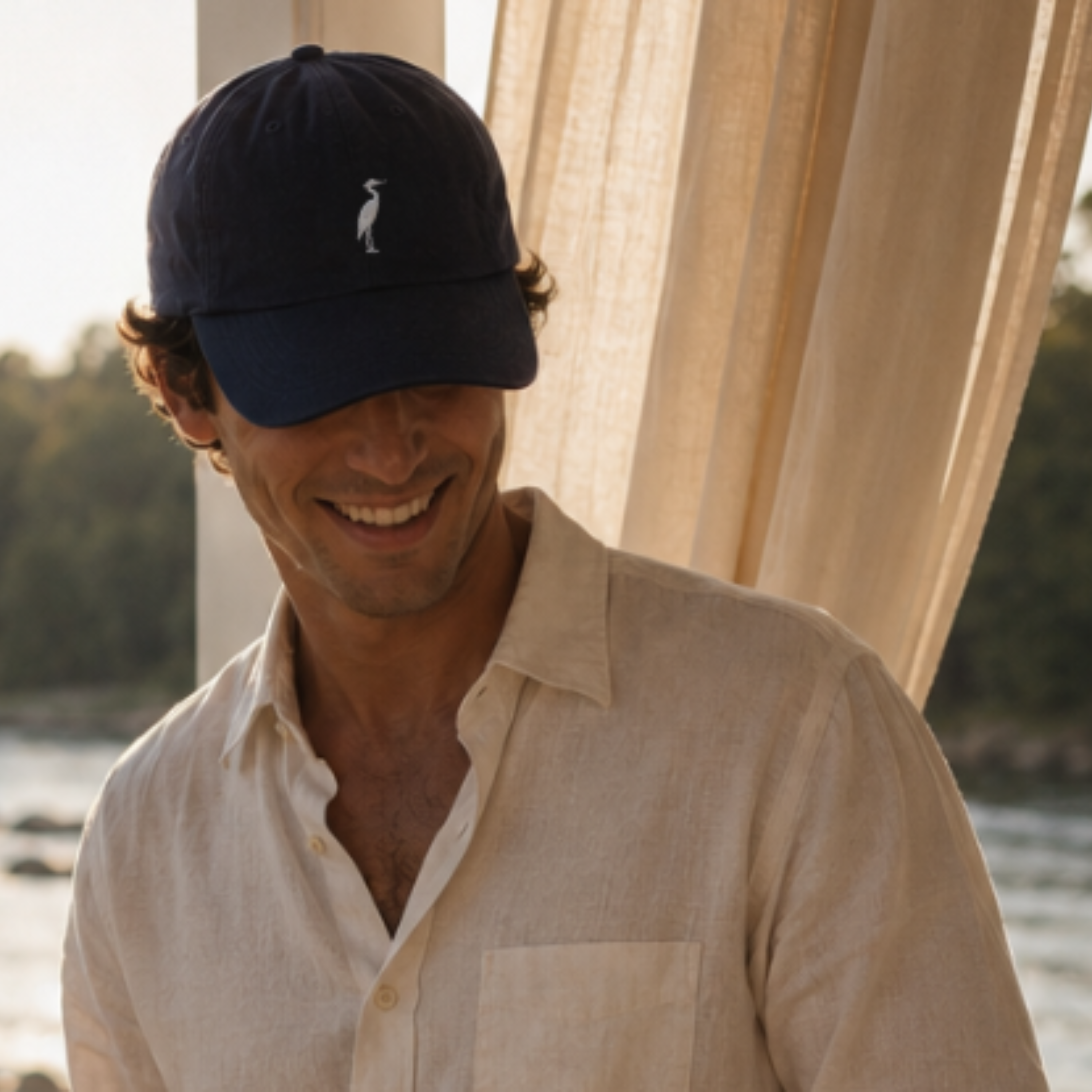 Blue Heron hat Richmond Virginia Man wearing a navy cap with a logo, smiling outdoors near a body of water.