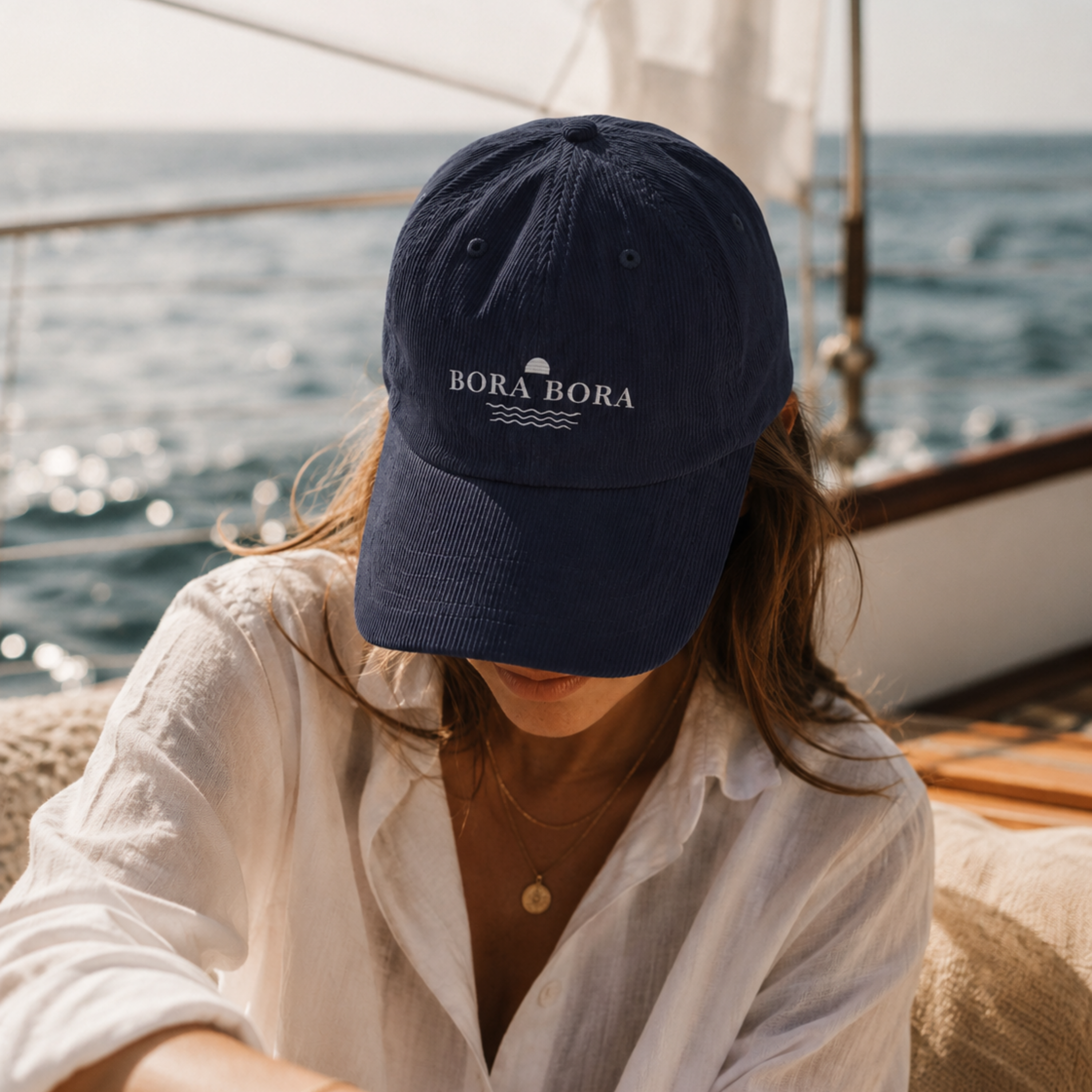 Person wearing a navy blue cap with 'Bora Bora' logo on a boat with ocean view