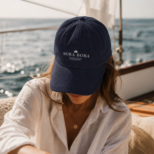 Person wearing a navy blue cap with 'Bora Bora' logo on a boat with ocean view