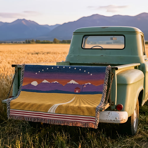 Amber Waves woven cotton throw over the tailgate of a vintage green pickup at the edge of a Montana wheat field