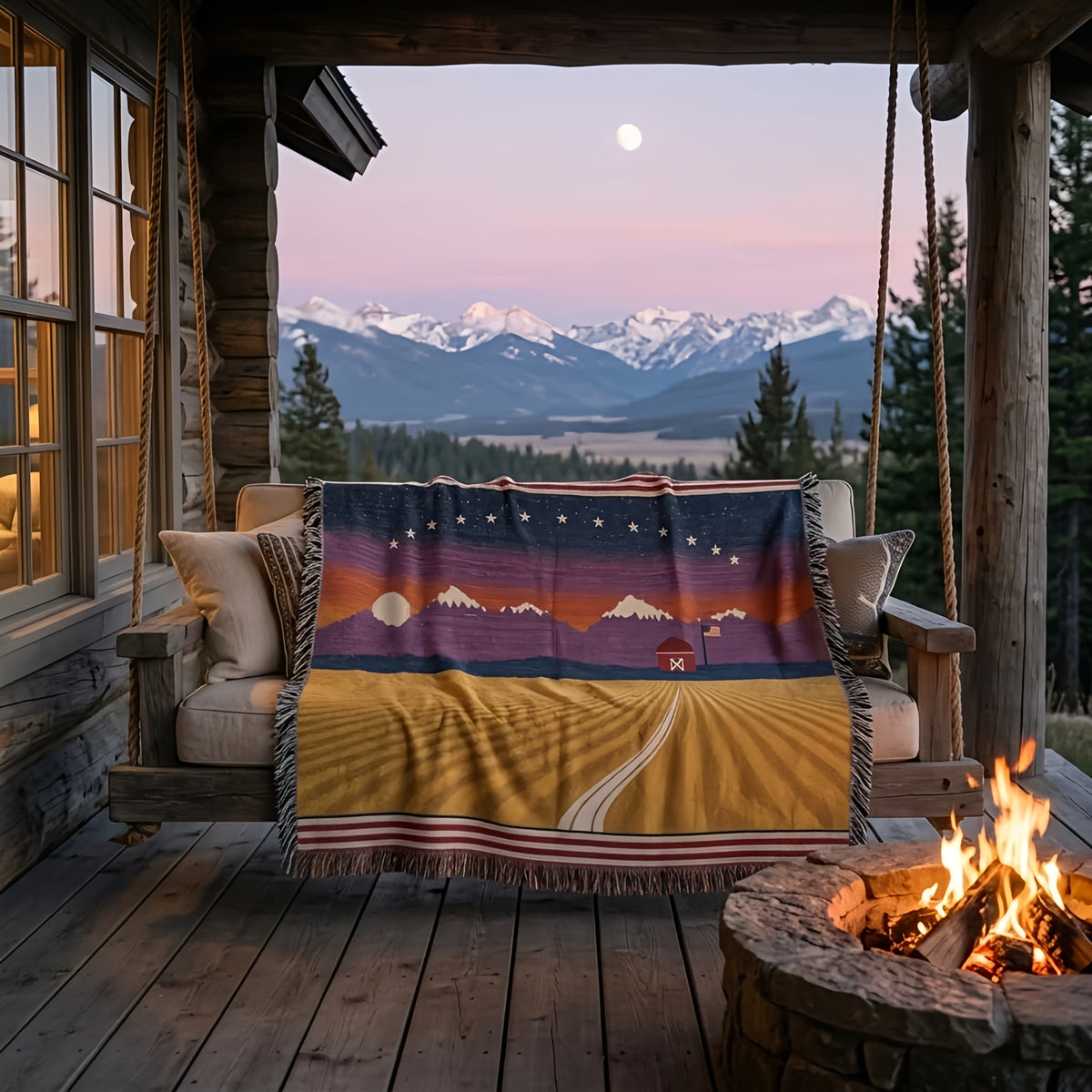 Amber Waves woven cotton throw on a cabin porch swing at dusk with snowcapped mountains, a full moon and fire pit