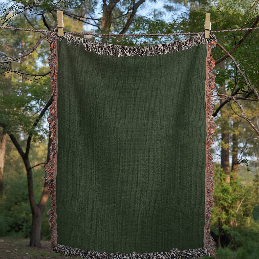 Solid hunter green woven cotton throw blanket, flat lay studio shot showing the uniform color, woven texture, multicolor side fringe, and black-and-white top and bottom fringe — Trini Skies