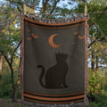Halloween Black Cat woven cotton throw blanket hanging outdoors between trees, showing the full black cat silhouette, crescent moon, and multicolor cotton fringe — Trini Skies