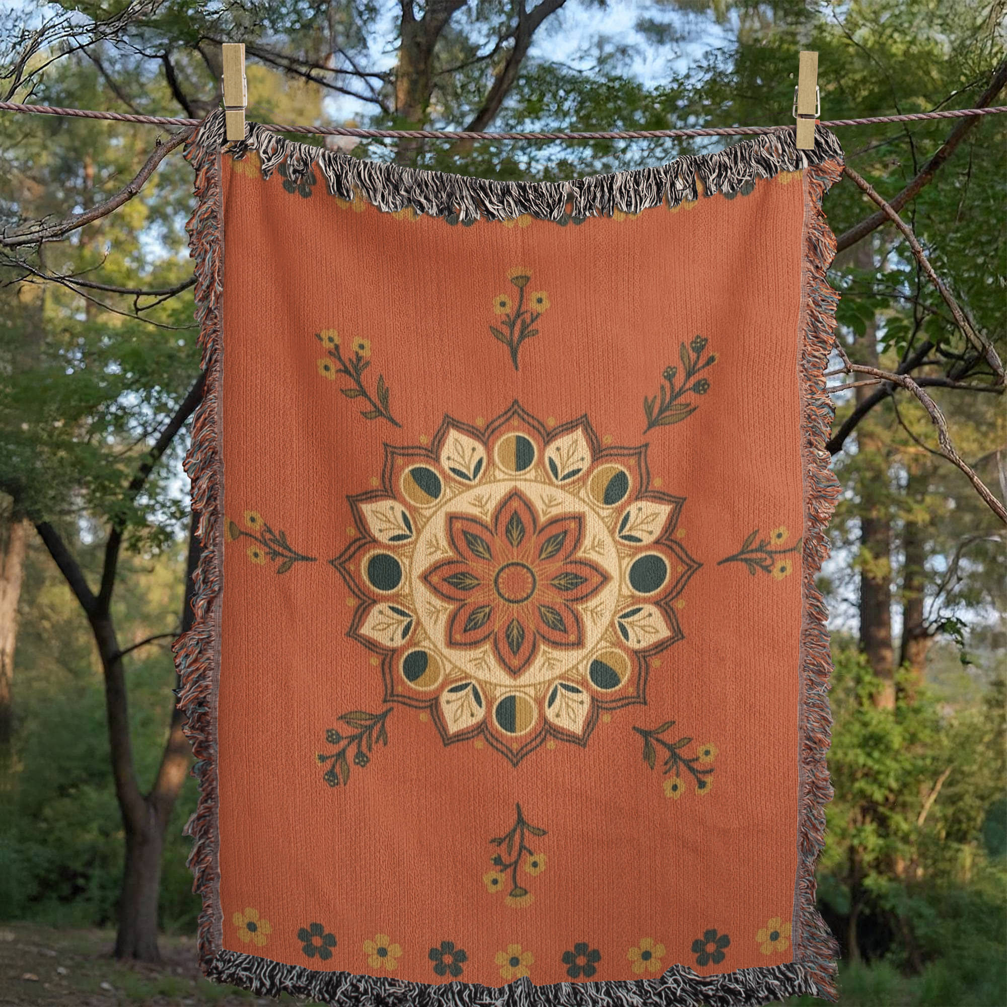 Moonflower moon phase mandala woven cotton throw blanket in coral with navy and gold accents, hung outdoors against trees, showing the jacquard weave and multicolor fringe — Trini Skies