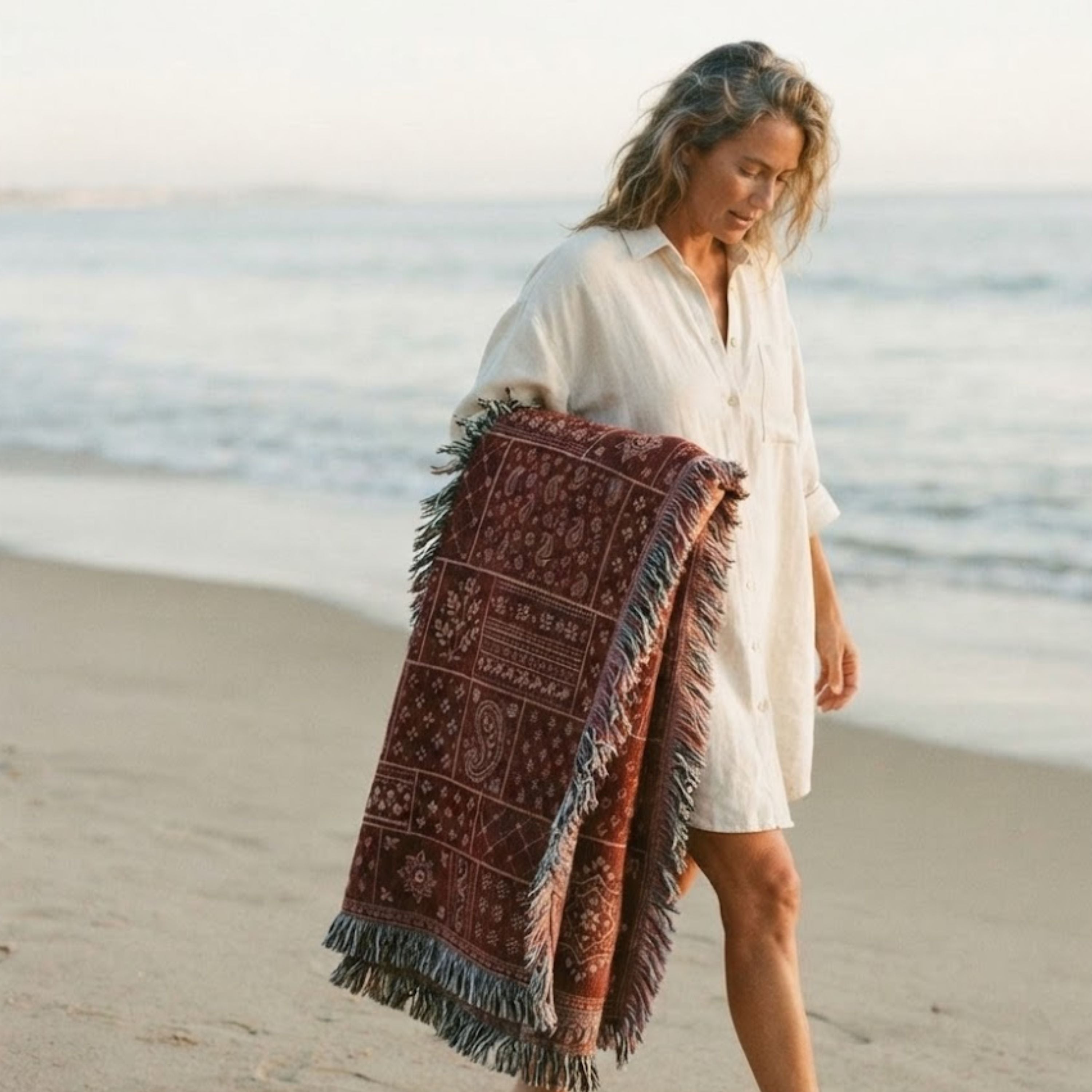 Woman wrapped in the Sundown Bandana paisley patchwork woven cotton throw blanket on the beach at sunset — Trini Skies