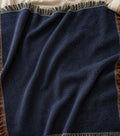 Solid deep navy woven cotton throw blanket, flat lay showing the uniform color, woven texture, multicolor side fringe, and black-and-white top and bottom fringe — Trini Skies