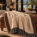 Oatmeal woven cotton throw blanket draped over an ottoman, showing the woven texture and confetti fringe — Trini Skies