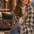 Woman wrapped in the Domino Onyx ivory and black plaid woven cotton throw blanket with fringe, sitting on a log cabin porch at golden hour
