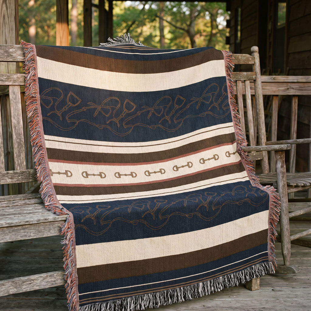 Stirrup Row equestrian woven cotton throw blanket draped over a porch chair overlooking a snowy mountain view, showing the navy and cream stripe pattern — Trini Skies