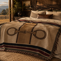 Equestrian Estate woven cotton throw blanket with snaffle bit motif styled on a log bed in a ranch bedroom — horse painting above, hunter green burgundy and navy stripe border, Trini Skies
