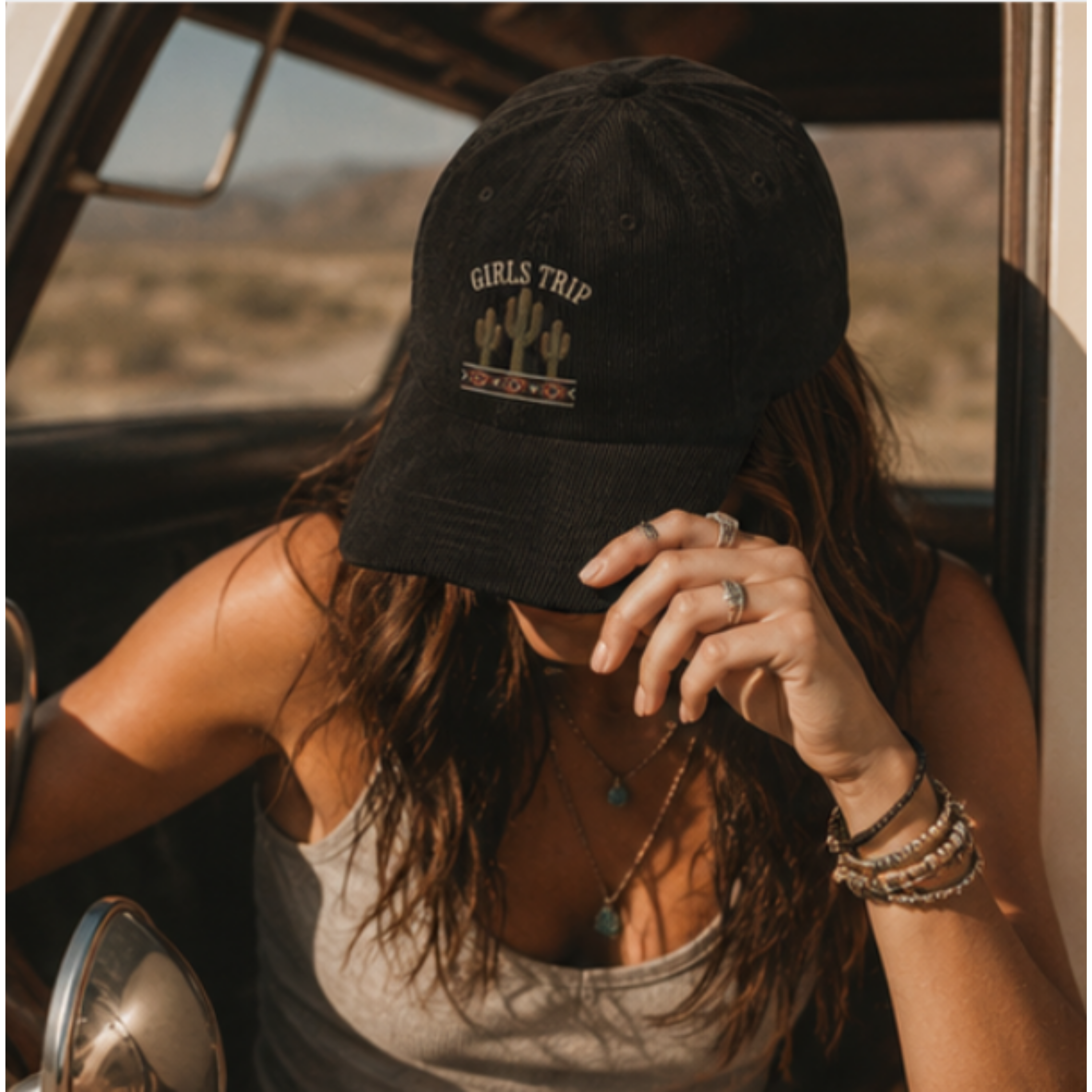 Person wearing a black 'Girls Trip' cap in a vehicle with a desert landscape in the background