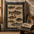 The Watershed multi-species fishing throw blanket on a rustic display rack, showing the full trout, bass, and lake trout design — Trini Skies