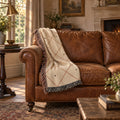 Diamond lattice woven cotton throw blanket in rust and cream draped over a dark green leather sofa