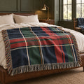 Navy, hunter green and red plaid woven throw across a bed in a dark paneled bedroom with ivory pillows and lamplight