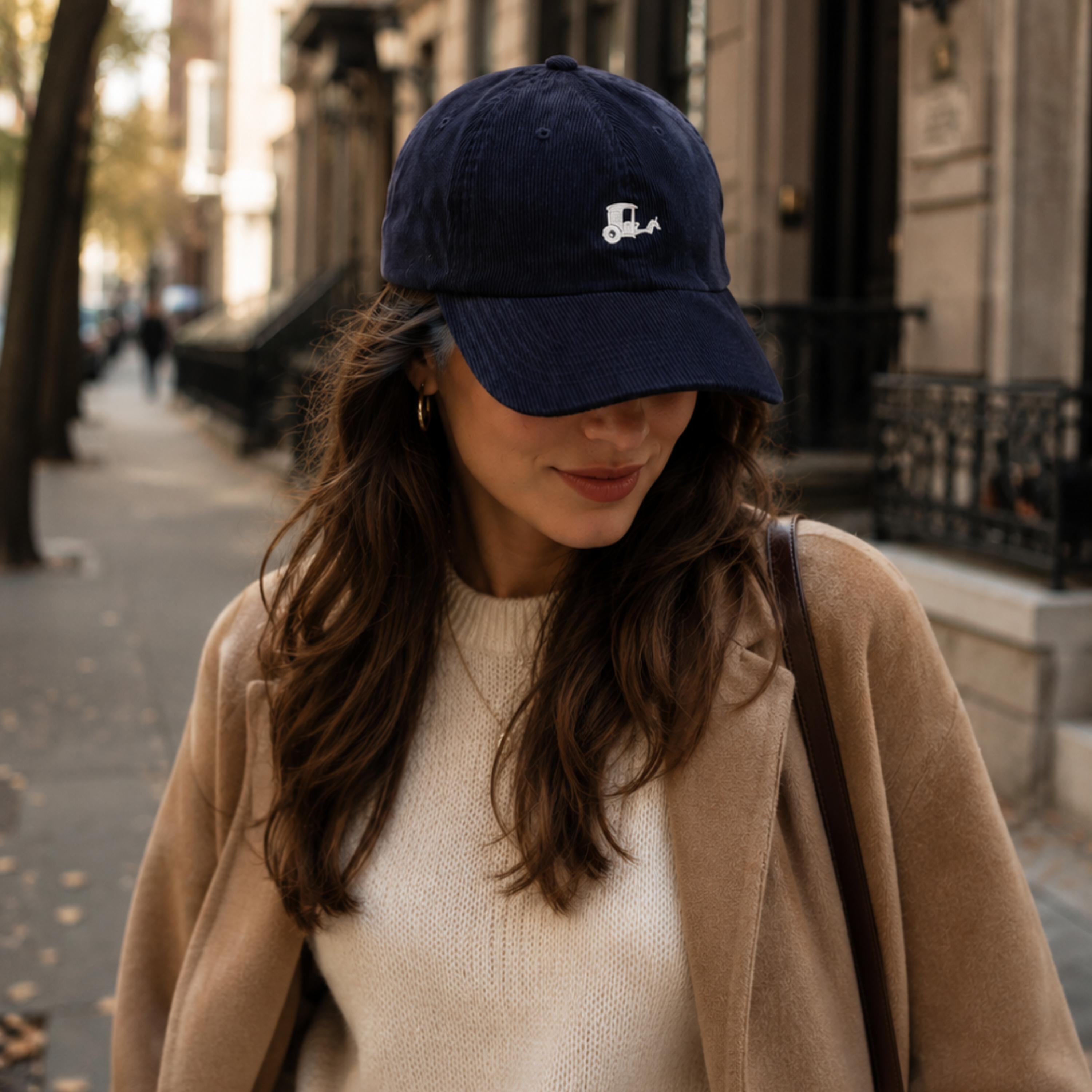Woman walking New York City street wearing navy New York Carriage corduroy hat camel coat autumn Trini Skies