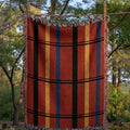 Red navy and gold plaid woven cotton throw blanket hanging outdoors on a clothesline showing full fringe detail and jacquard weave texture — Trini Skies