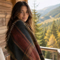 Woman wrapped in the Ember Ridge woven plaid throw overlooking a forested valley — Trini Skies