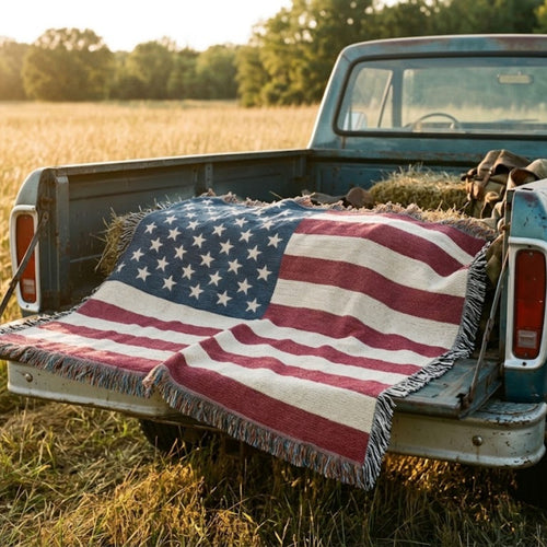 50-star American flag cotton throw over the tailgate of a vintage blue pickup with hay bales in a field