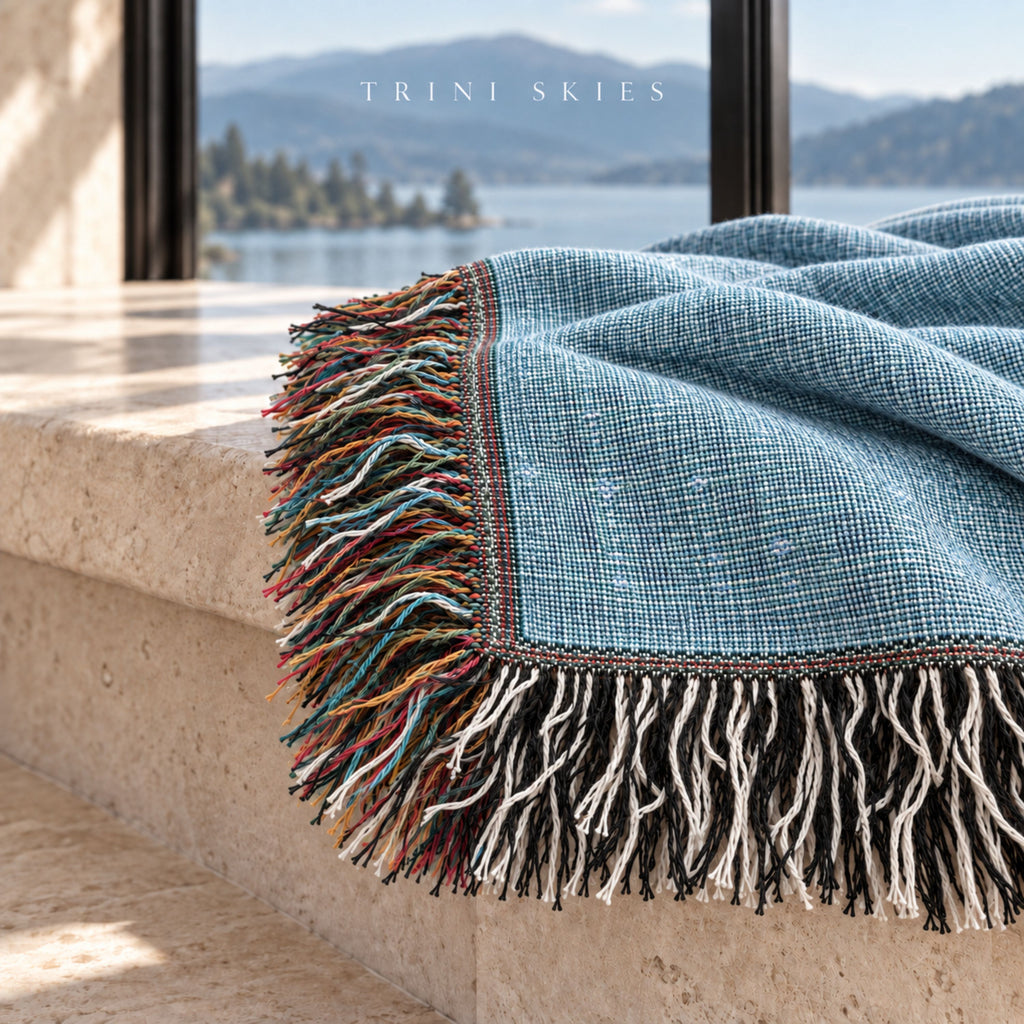 Chambray blue solid woven cotton throw blanket draped over a stone ledge with a lake view