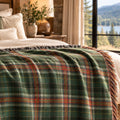 Green plaid woven cotton throw blanket draped over a bed with a mountain lake view