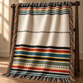 Rust, teal, olive, and gold striped woven cotton throw blanket with fringe on a wooden ladder rack