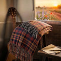 Denim and rose plaid woven cotton throw blanket with multicolor tassel fringe draped over a guitar